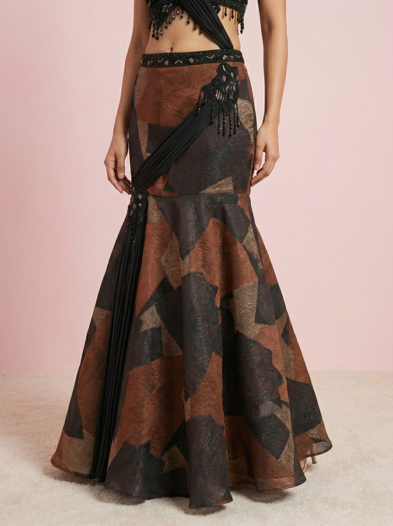 Long, patterned, mermaid style skirt worn by a model on a light pink background