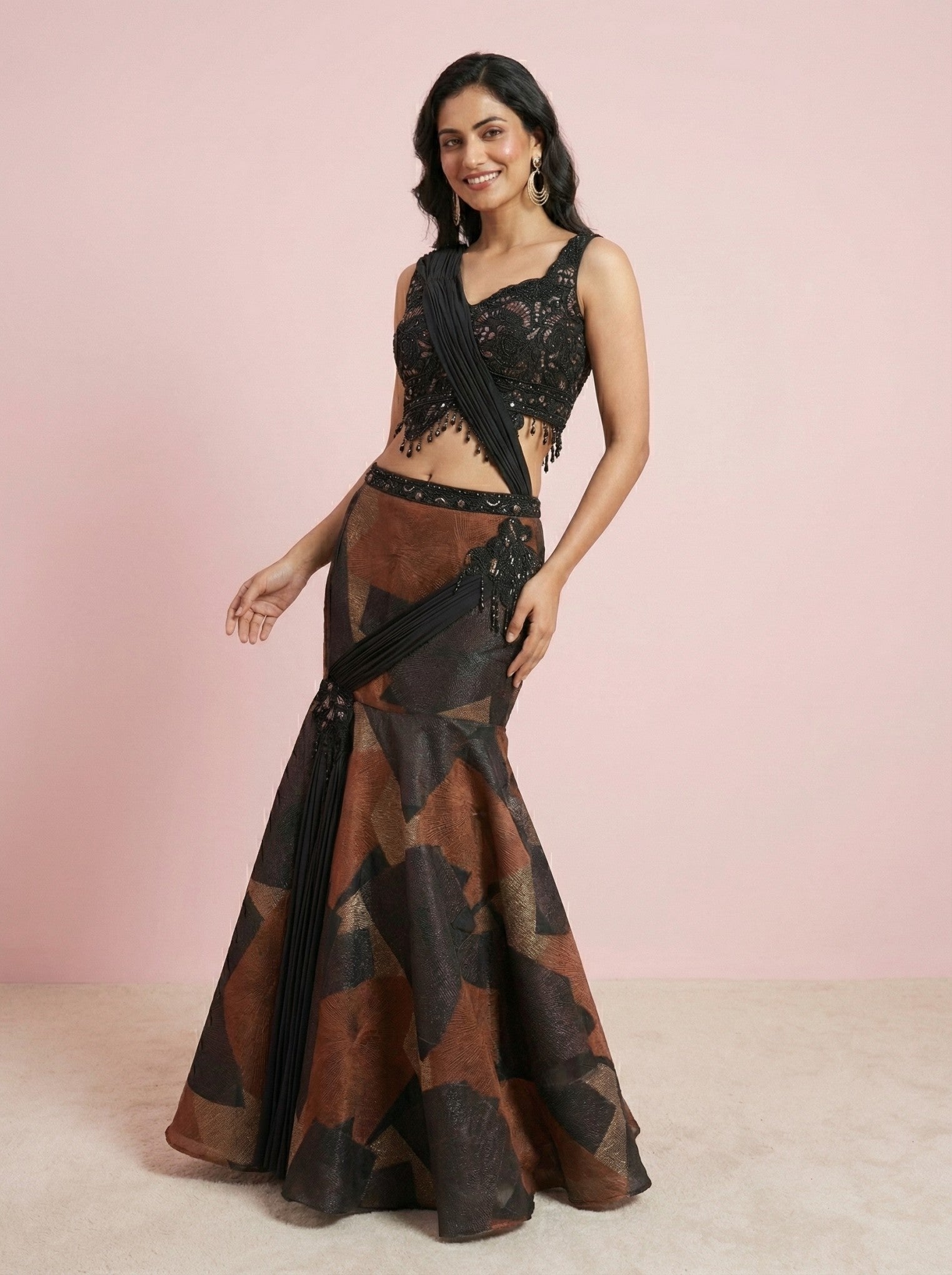 Woman wearing a black and brown mermaid style lehenga smiling with a pink background