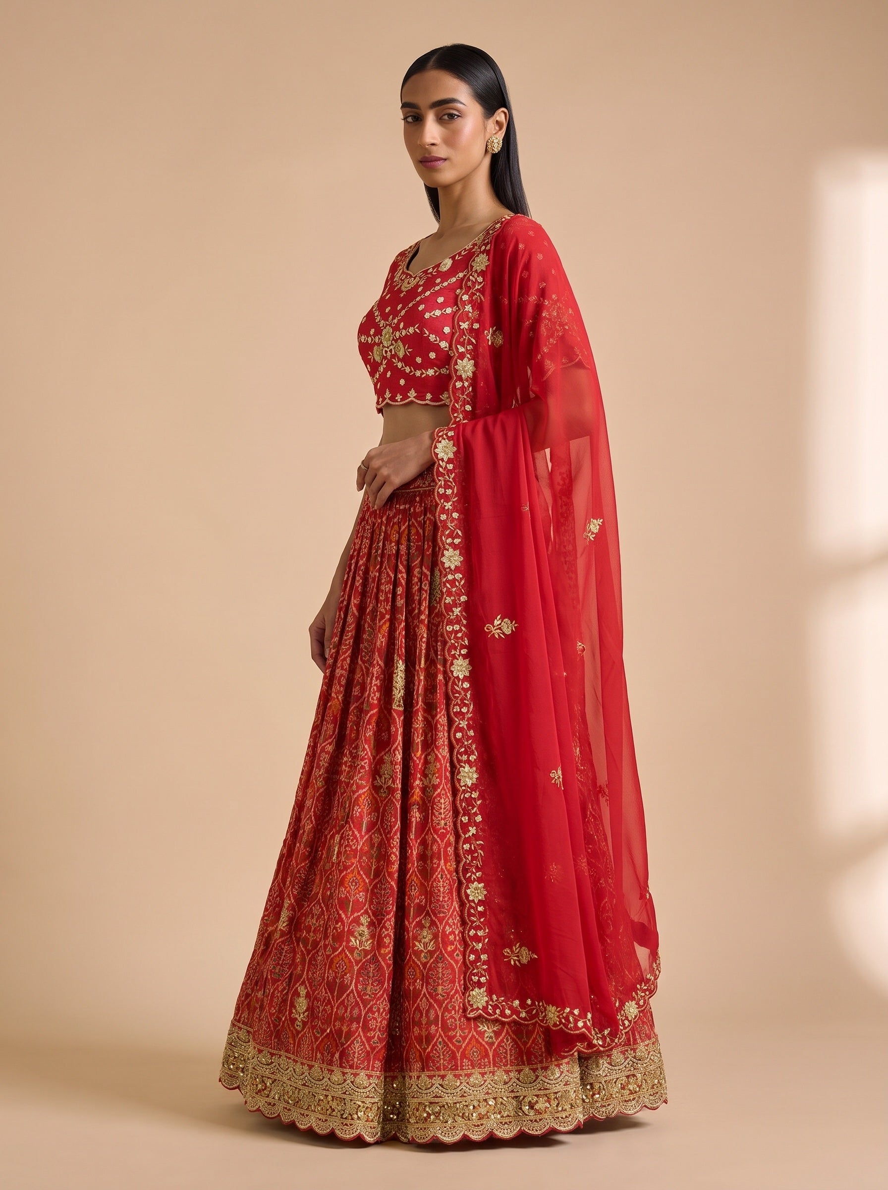 Three-quarter view of red silk lehenga showing the patterned skirt, embroidered blouse and scalloped border